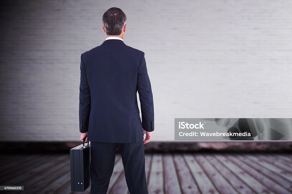 Composite image of businessman in suit holding a briefcase Businessman in suit holding a briefcase against grey room Briefcase Stock Photo