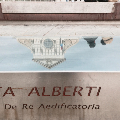 Florence, Italy - February 15, 2014: Leon Battista Alberti, an Italian artist and architect who lived in the 15th Century, designed the facade of Santa Maria Novella's Church in Florence. Today, in the square where the Church is located, some public benches, some of which covered with with glass panes, bear his name and some Latin inscriptions describing his works. The photograph shows the reflection of the Church into one of these benches. 