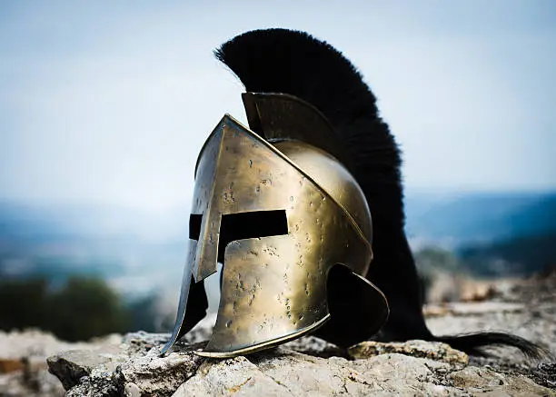 Spartan helmet with black crest on rocks.