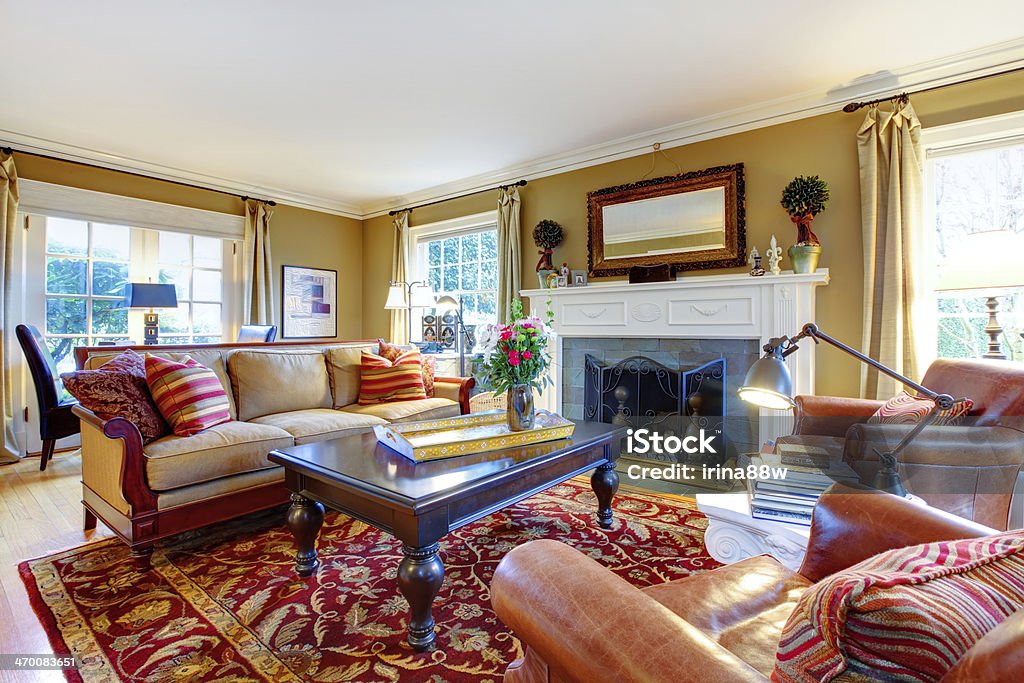 Charming family room with old style furniture and fireplace Cozy family room with light tone walls,  old-fashioned furniture, marble table, classic red rug and stoned background fireplace Architecture Stock Photo