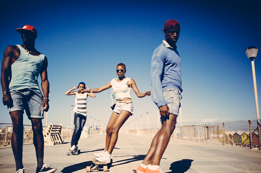 Group of cool African American teenagers casually longboarding at the beach on a wide walkway