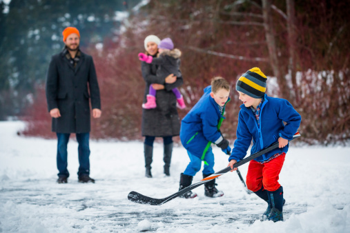 Young family playing pond hockey outside in the snow.