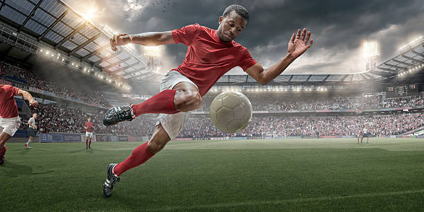 Soccer Hero In Action A close up image of a professional football player in mid air about to control football during a soccer game. The action occurs on a outdoor soccer pitch in a generic floodlit soccer stadium full of spectators under a stormy evening sky at sunset. All players are wearing generic football kit. soccer striker stock pictures, royalty-free photos & images