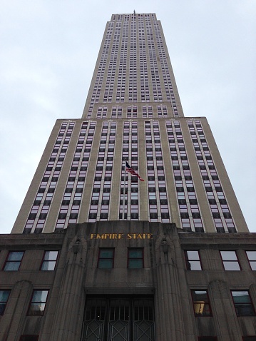 A vertical panoramic photograph of the Empire State Building, seen from across the street of the front door.