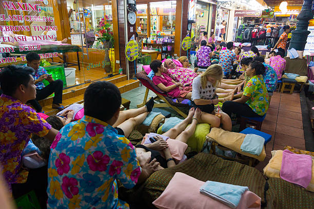 Bangkok, Thailand - March 11, 2015: Tourists are sitting outside of massage shop in second part of Khaosan Road at night and are getting foot massage. Thai people are doing massage. Other tourists are standing in street.