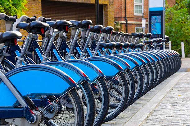 Bicycles lined up in a row in London, England City Bike Rental - Stock Image, a row of bikes for hire as part of a new scheme to encourage "pedal power" in the City of London. The aim is to reduce dependance on cars and thereby reduce London's polution, emission of greenhouse gases, conserve energy and of course to promote a healthier lifestyle. Sponsor's branding carefully removed. bicycle docking station stock pictures, royalty-free photos & images