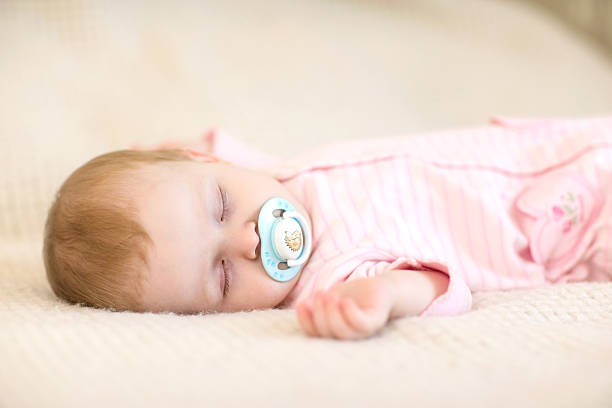 Cute little baby girl sleeping with a soother on the bed