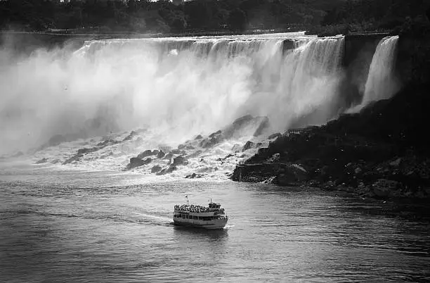 A view of the tourist boat at Niagara Falls with mist coming off the American side of Niagara Falls in black and white.