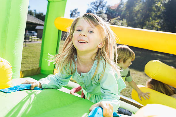 kleines mädchen mit lustigen klettermöglichkeiten auf einem bounce house - house bouncing multi colored outdoors stock-fotos und bilder