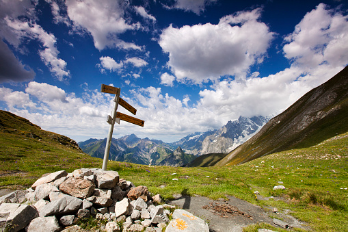 Road Sign in mountain landscape on the Tour du Mont Blanc, Ferret Valley, Valle d'Aosta, Italy with cloudy sky. Mountains in the background. Shot with a wide angle lens on a Canon 5D mark II. Low ISO for sharpness.