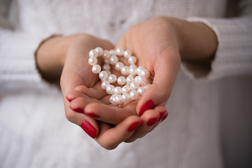 Pearls in female hands with red manicure