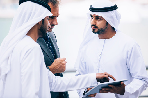 Emirati and Western businessmen checking content on a tablet and explaining something to each other.