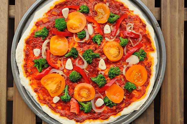 Raw round pizza with yellow cherry tomatoes, onion, garlic