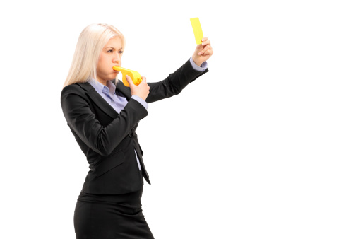 Young businesswoman blowing a whistle and showing a yellow card, isolated on white background