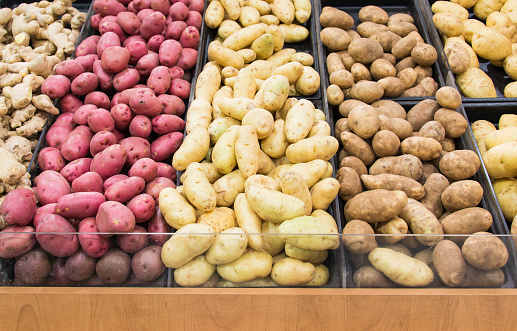 Grocery store displays different colors and varieties of potatoes for people to select their favourite, agricultural produce arranged in lines.