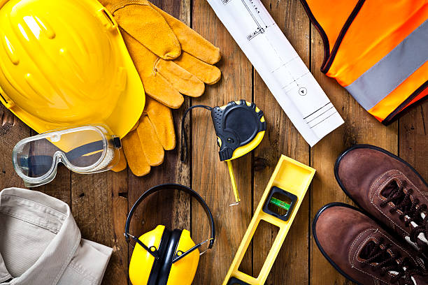 Personal safety workwear and construction blueprint shot directly above Personal protective workwear and blueprint with some measuring instruments shot directly from above on rustic wood background. The protective workwear includes hard hat, gloves, earmuff, goggles, steel toe shoes, and safety vest. The composition also includes a tape measure and bubble level and a construction blueprint, all items used by construction worker or engineer. Predominant colors: yellow and brown. protective glove photos stock pictures, royalty-free photos & images