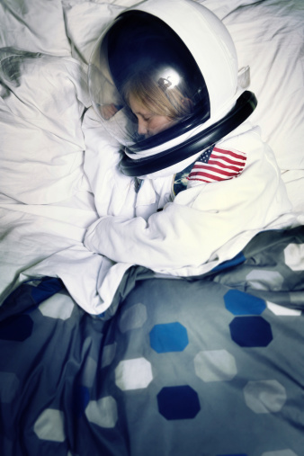 This is a photo about reaching your dreams using the concept of a young boy in a space suit sleeping in his bed.