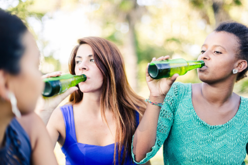 Three young women relaxing at the park, drinking beers.