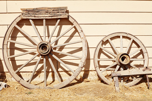 Two old faded wooden wheels leaning up against wooden wall under bright summer sunlight