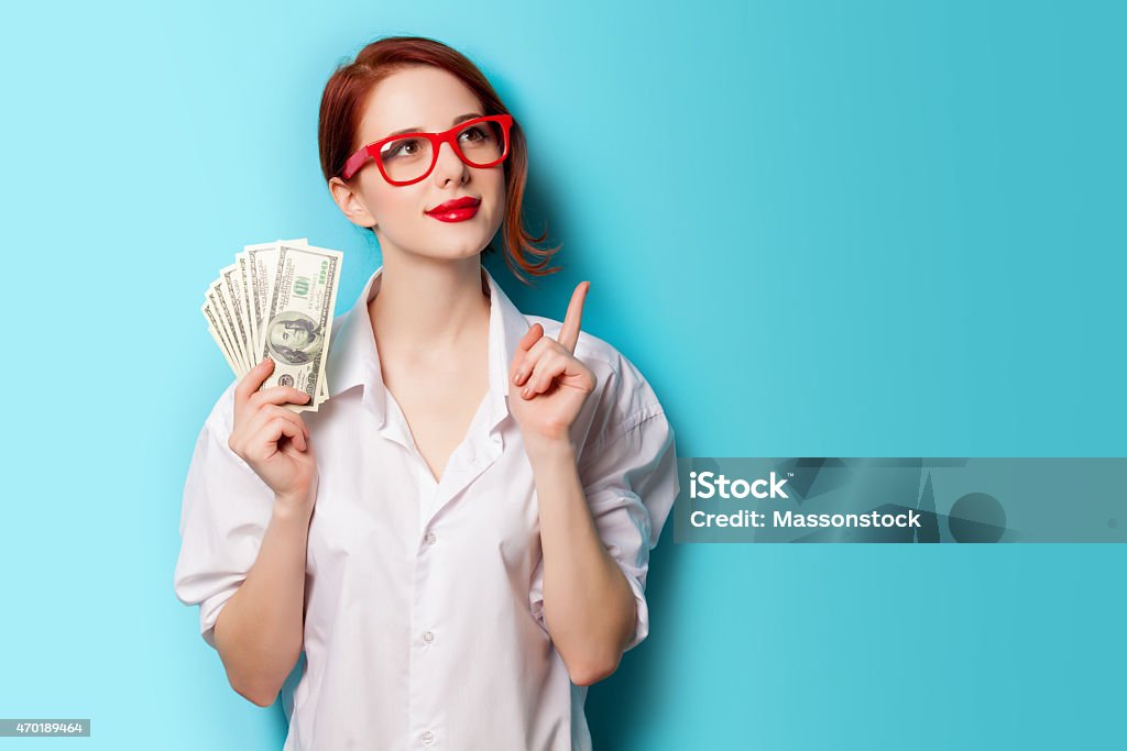 Woman wearing red glasses with money in her hand Portrait of redhead women in red glasses with money on blue background Currency Stock Photo