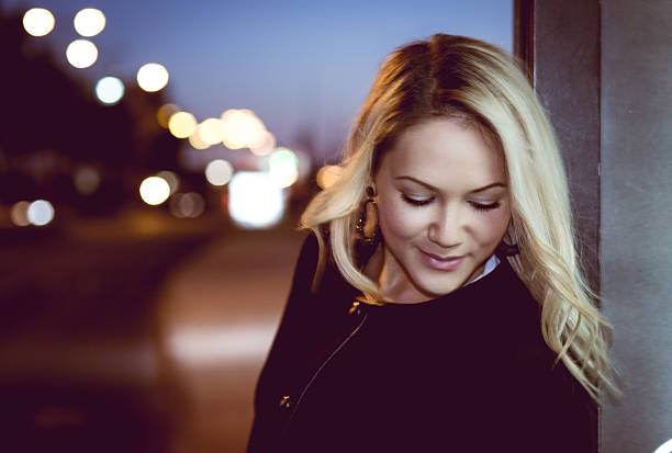 Beautiful blonde woman in black classic coat waiting on the night road background