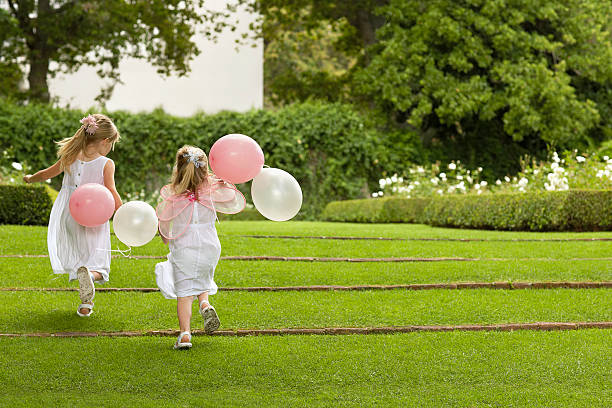 Bridesmaids With Balloons Running In Garden stock photo
