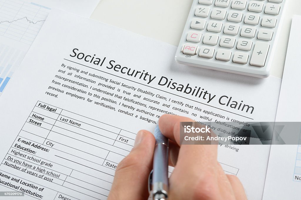 Person Hand With Pen Filling Social Security Disability Form Close-up Of Person Hand With Pen And Calculator Filling Social Security Disability Claim Form Claim Form Stock Photo