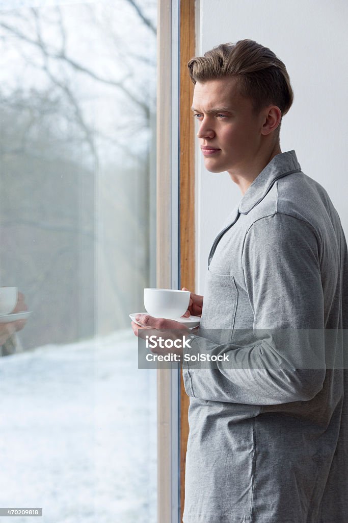 Cup of Coffee in the Morning Mean looking young man wearing in pyjamas, standing against white wall holding cup of coffee. Image is strongly lit by sunlight. 20-29 Years Stock Photo
