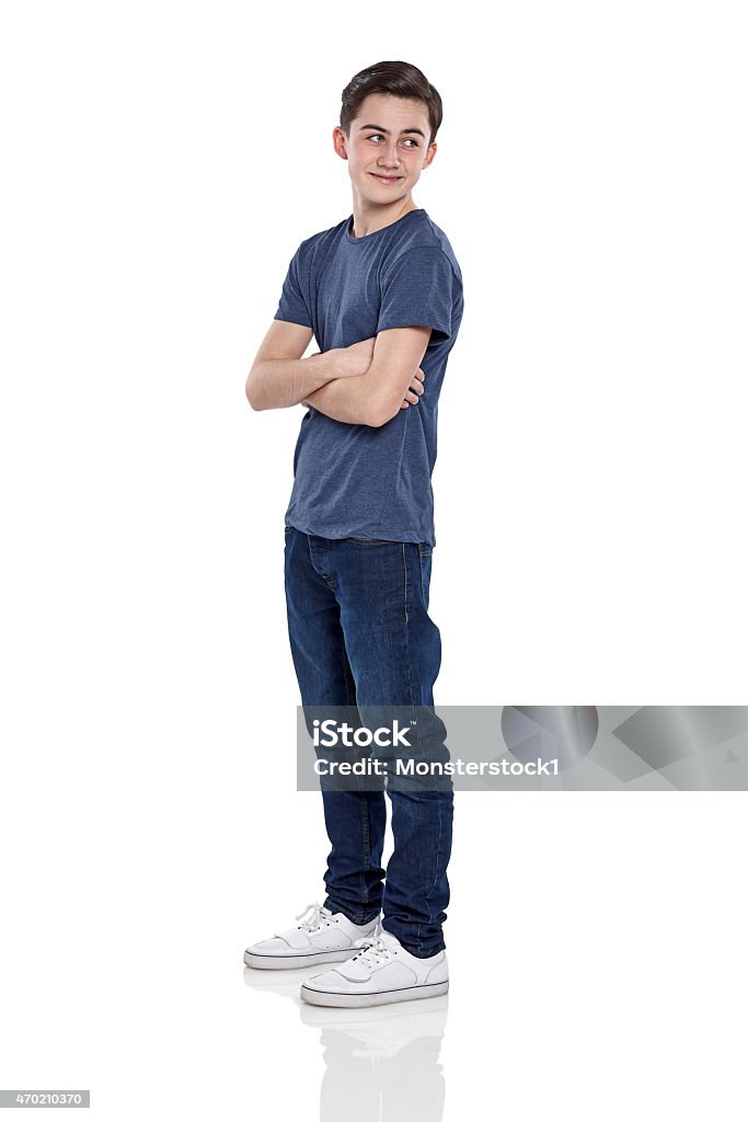 Happy young boy looking over shoulder Full length portrait of happy young boy standing with his arms crossed looking over shoulder against white background Boys Stock Photo