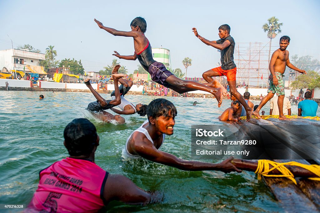 Young men diving in pool, Mahabalipuram, India Mahabalipuram, India - March 14, 2014: Young men are playing on the bank of a pool in a small village close to Mahabalipuram, during a local Hindu Festival. 2015 Stock Photo