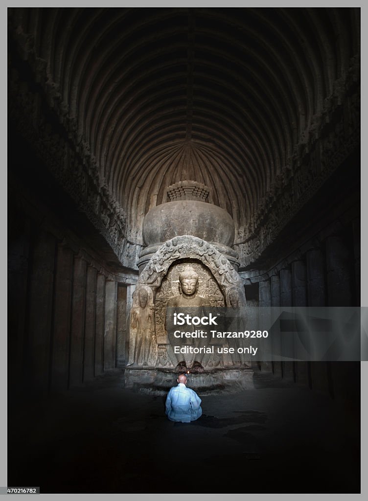 Monk sitting in front of Buddha statue, Ellora Caves, India Aurangabad, India - February 26, 2014: A monk is sitting in front of a buddha statue in the 16th cave, Ellora Caves, India. Cave Stock Photo