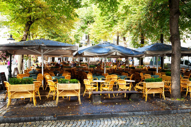 Maastricht, The Netherlands - September 18, 2014: Capture of restaurant tables at square Onze Lieve Vrouweplein in Maastricht at summer. Some people are sitting at tables in background. Waiter is walking around. Some trees are on sqaure. Other people are walking in street at left side.