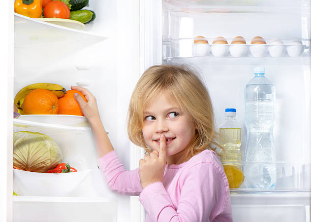 istock Little cute girl making silence sign near open fridge 470220736
