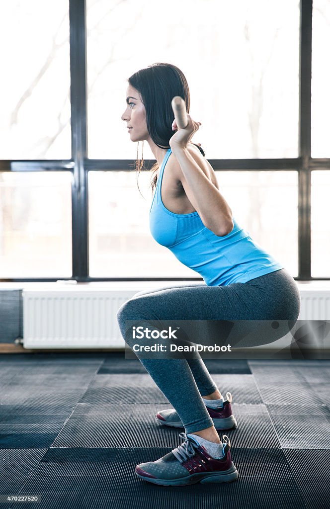 Young woman doing squats with barbell Side view portrait of a young woman doing squats with barbell at fitness gym 2015 Stock Photo