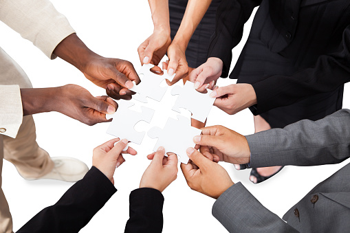 Cropped image of business people's hands solving jigsaw puzzle over white background