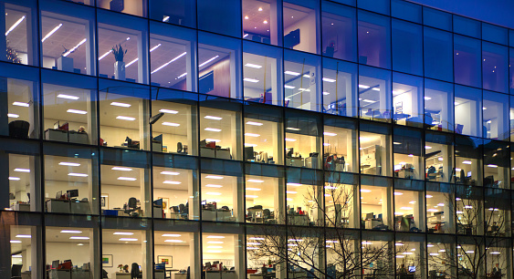 London, UK - December 19, 2014: Office block with lots of lit up windows and late office workers inside. City of London business aria in dusk.