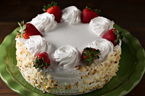 An extreme close up horizontal photograph of a tres leeches (three milks) cake decorated with ripe red strawberries. The cake derives it's name because it is soaked in evaporated milk, condensed milk and cream.