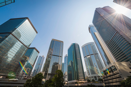 Bright sunlight bursting through the glass canyons of skyscrapers and dowtown business towers as they reach for clear blue skies, Hong Kong, China. ProPhoto RGB profile for maximum color fidelity and gamut.