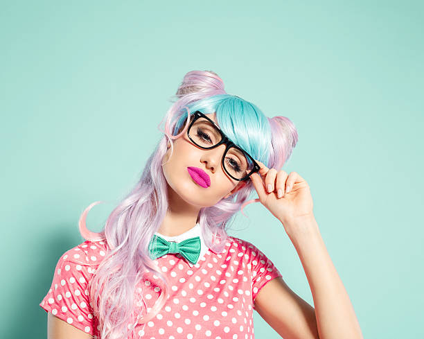 Pink hair manga style girl holding nerd glasses Portrait of confident manga style blue-pink hair young woman wearing pink polka dot dress with collar, bow tie and nerd glasses. Standing against turquoise background, looking at camera. Studio shot, one person. nerd stock pictures, royalty-free photos & images
