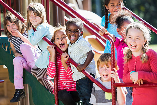 grand groupe de multi ethnique enfants sur un terrain de jeux ensoleillé - playground schoolyard playful playing photos et images de collection