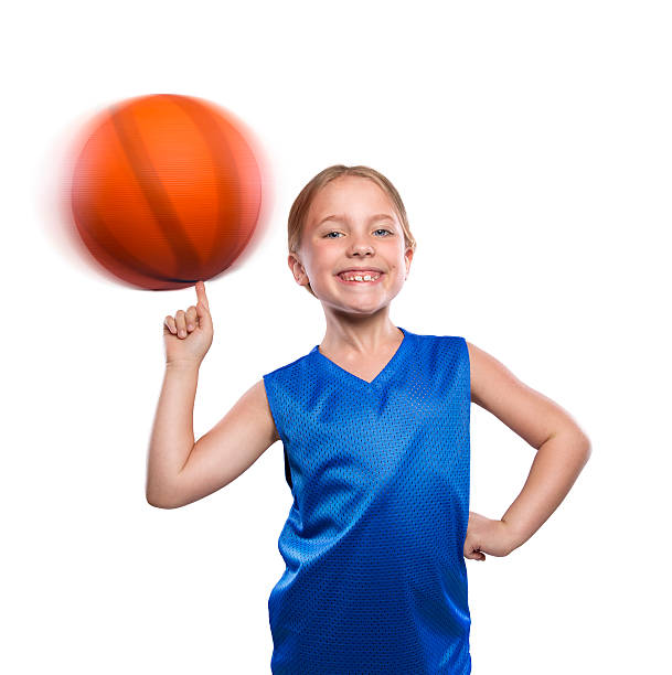 A elementary age female basketball player spinning a basketball on her finger on a white background.  The blond caucasian  girl is wearing a blue basketball jersey and is isolated on a white background.  Please see my portfolio for other images of this model.  