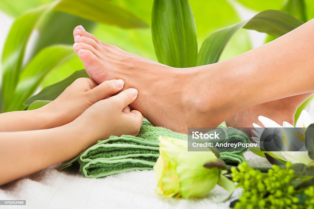 Masseuse Massaging Woman's Foot Against Leaves Cropped image of masseuse massaging woman's foot against leaves at spa 2015 Stock Photo