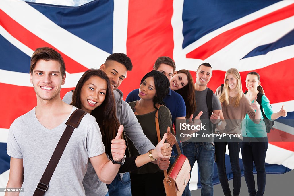 A English flag and a diverse group of people Group Of Happy Multi Ethnic Students Standing In Front Of Uk Flag Showing Thumb Up English Culture Stock Photo