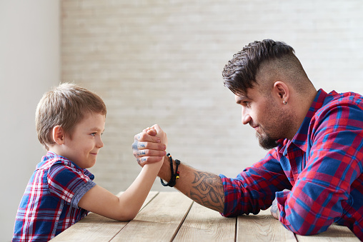 Father and little son competing in arm wrestling