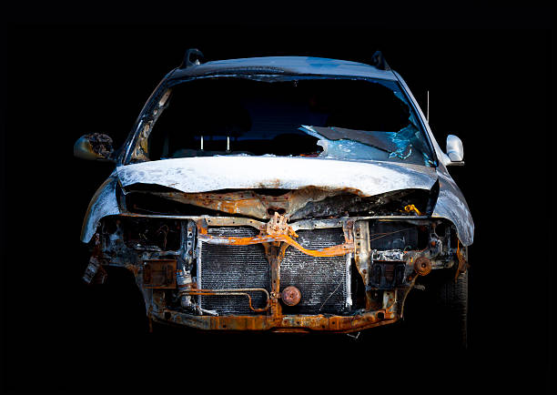 Front view of burnt down rusty car wreck isolated on black background, full frame horizontal composition with copy space and clipping path included