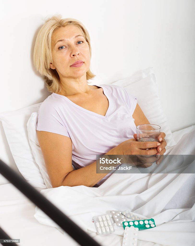 Serious female pensioner taking medicine Serious female pensioner taking medicine before falling asleep 2015 Stock Photo