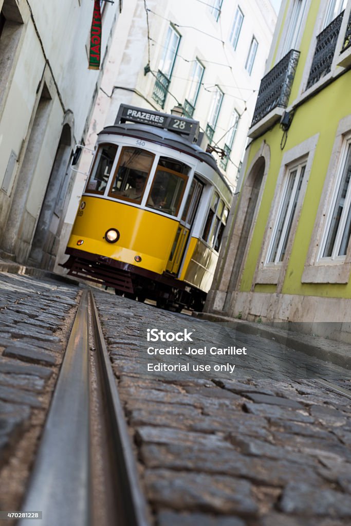 Tram on narrow cobblestone street in Lisbon, Portugal Lisbon, Portugal - June 17, 2014: A yellow tram #28 navigates the narrow cobblestone streets in the Alfama district of Lisbon, Portugal. The driver is visible in the window. 2015 Stock Photo