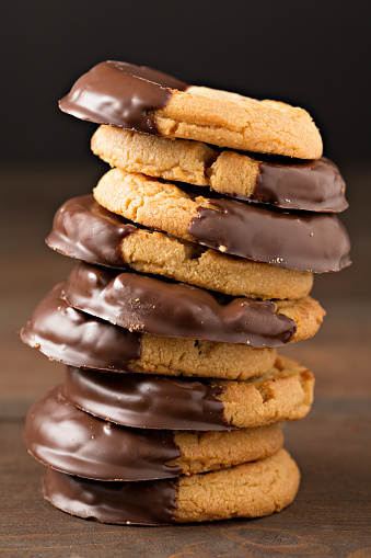 An extreme close up vertical photograph of a precariously balanced stack of chocolate dipped peanut butter cookies,