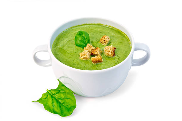Green soup puree in a white bowl with croutons and spinach leaves isolated on white background