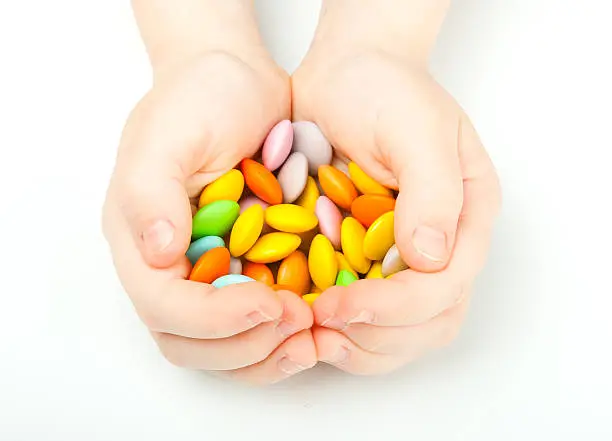 Children's hands holding colorful candy on white background